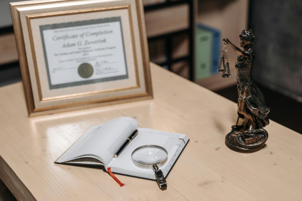 A framed certificate with Lady Justice statue on a wooden desk.